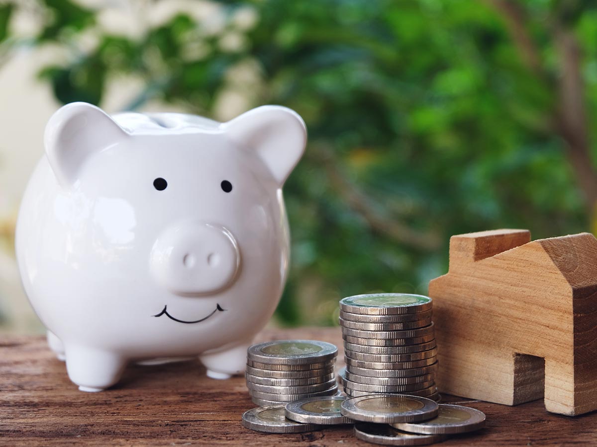 Piggy bank on a wood table next to money and a small wood house